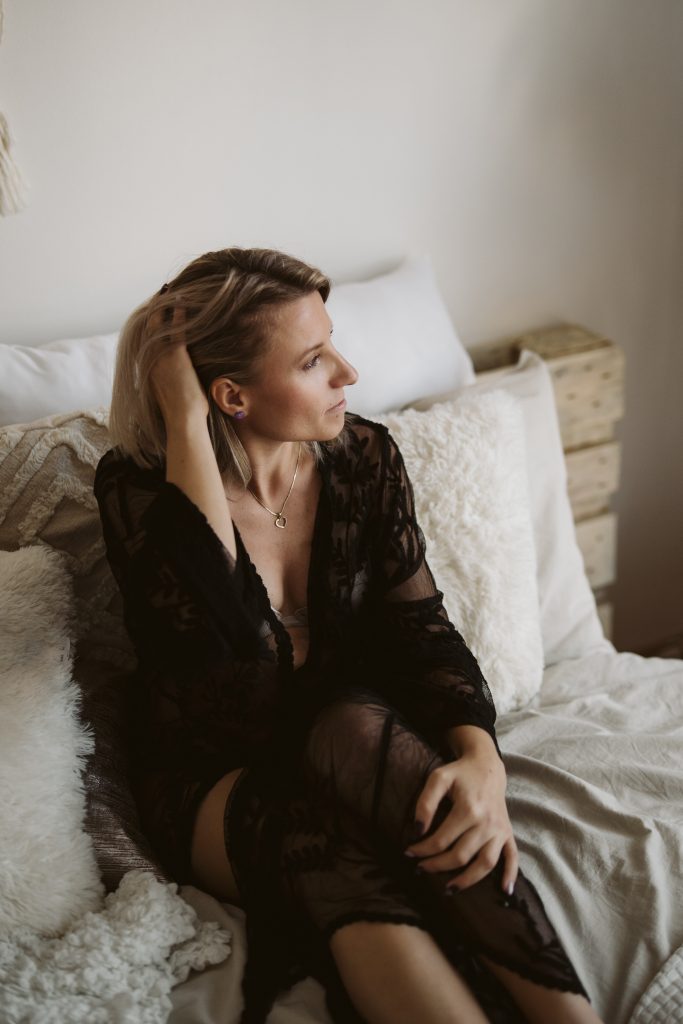 Portrétní foto ženy v černých krajkových šatech na posteli v ateliéru