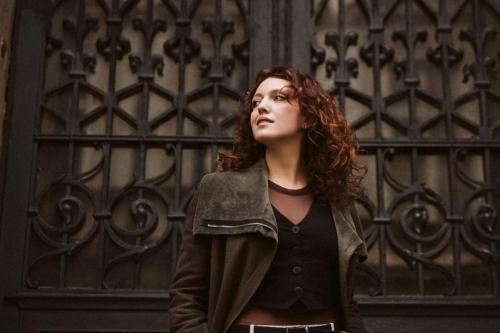 Portrét dívky s rezavými vlnitými vlasy před kovovými dveřmi