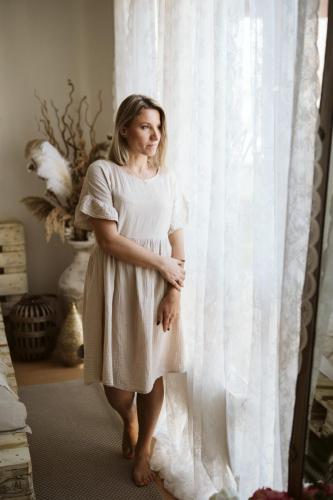Fotografie ženy dívající se z okna v krátkých béžových šatech